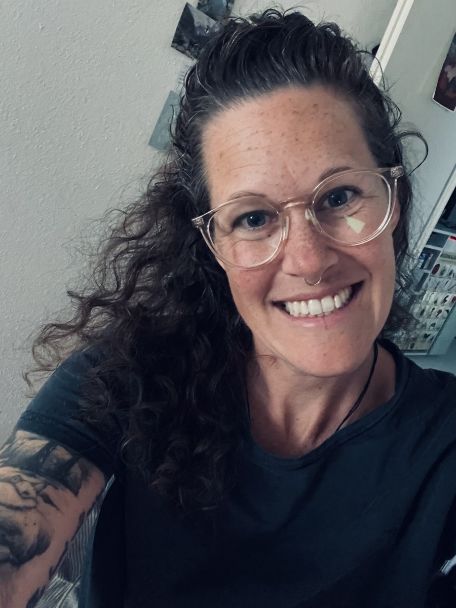 Porträt von Eveline – lächelnd, mit lockigem Haar und heller Brille